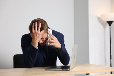 Photo of Young businessman with laptop complaining to someone via phone at wooden table indoors, space for text