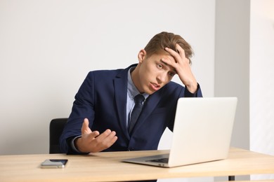 Photo of Young businessman with laptop complaining to someone via phone at wooden table indoors