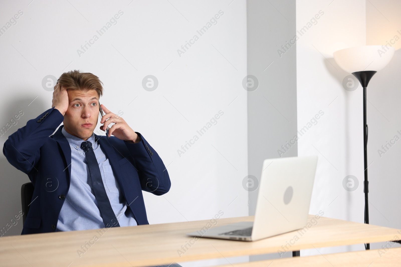 Photo of Young businessman with laptop complaining to someone via phone at wooden table indoors