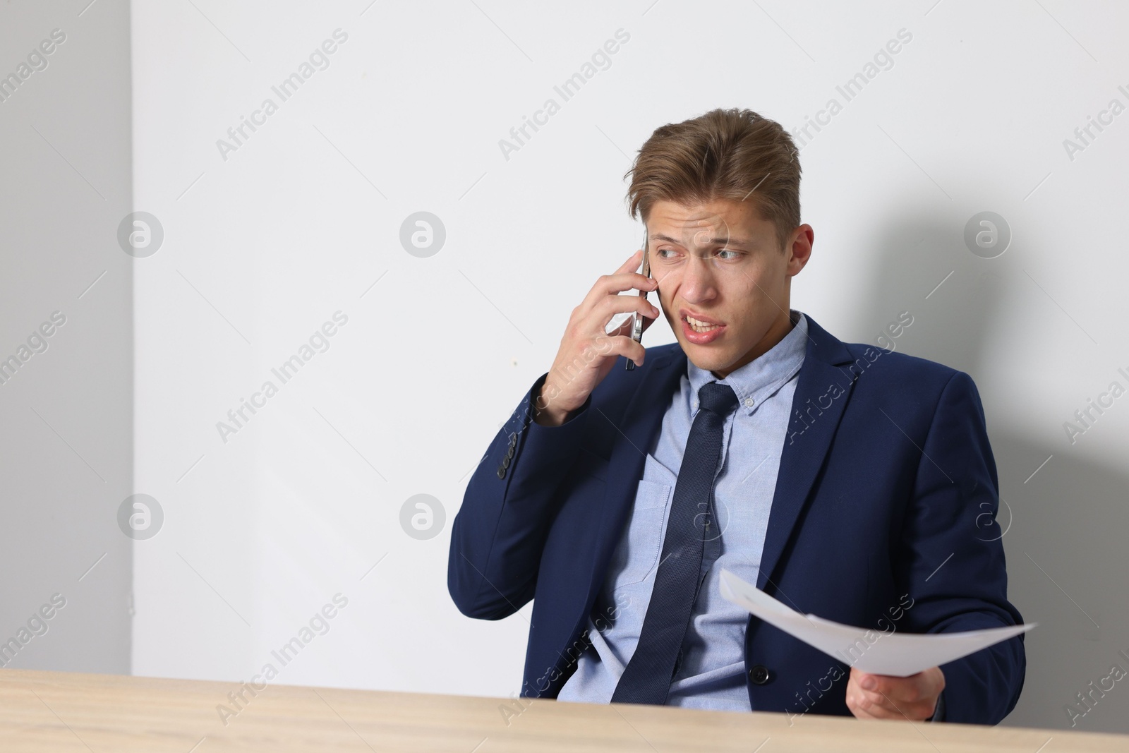 Photo of Young businessman with papers complaining to someone via phone at wooden table indoors, space for text