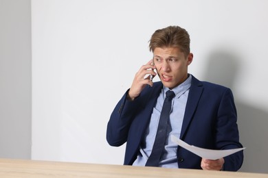 Photo of Young businessman with papers complaining to someone via phone at wooden table indoors, space for text