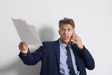 Photo of Young businessman with papers complaining to someone via phone indoors