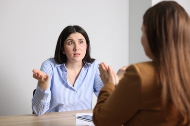 Photo of Young woman complaining to businesswoman at wooden table indoors