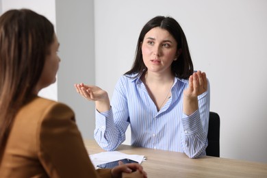 Photo of Young woman complaining to businesswoman at wooden table indoors
