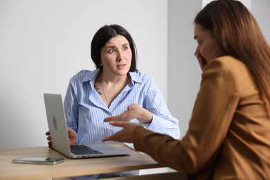 Photo of Young woman complaining to businesswoman at wooden table indoors