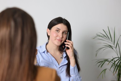 Photo of Young woman with phone complaining to businesswoman indoors