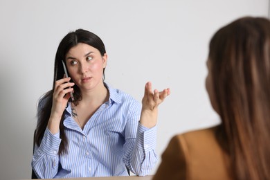 Photo of Young woman with phone complaining to businesswoman indoors