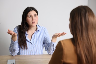 Photo of Young woman complaining to businesswoman at wooden table indoors