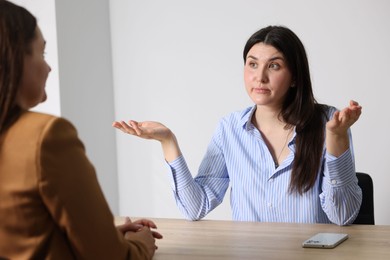 Photo of Young woman complaining to businesswoman at wooden table indoors
