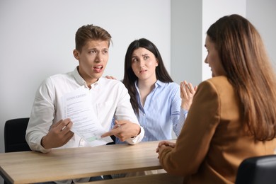 Photo of Couple complaining to woman at wooden table indoors