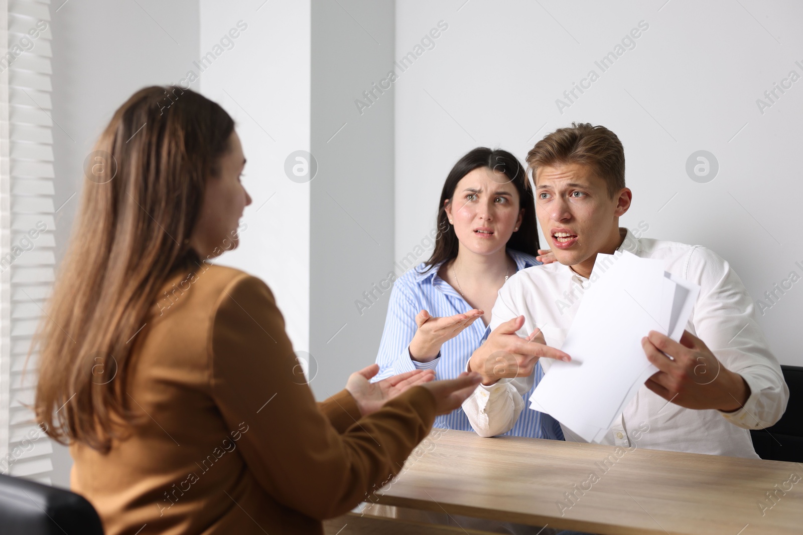 Photo of Couple complaining to woman at wooden table indoors