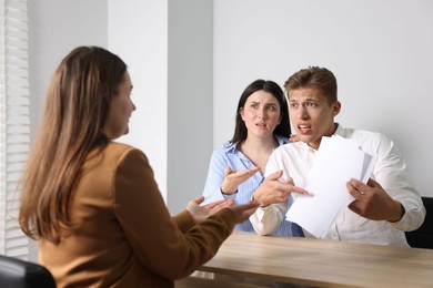 Photo of Couple complaining to woman at wooden table indoors