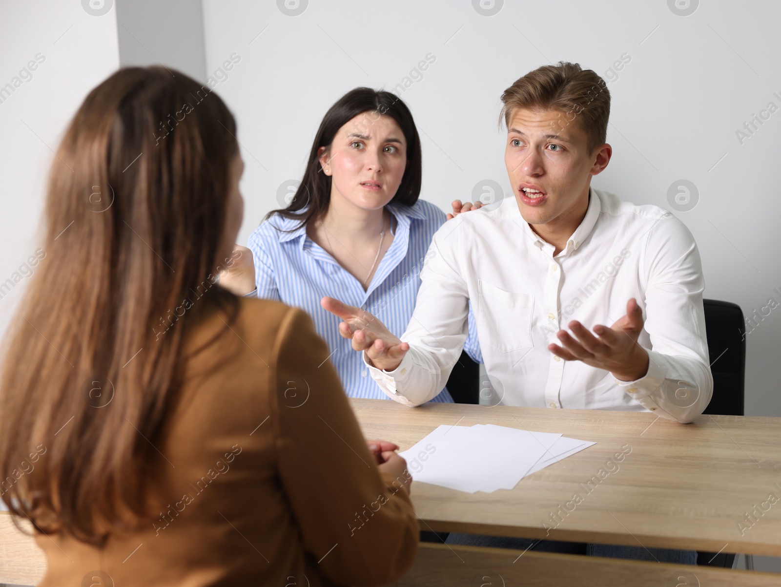 Photo of Couple complaining to woman at wooden table indoors