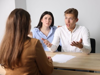 Photo of Couple complaining to woman at wooden table indoors