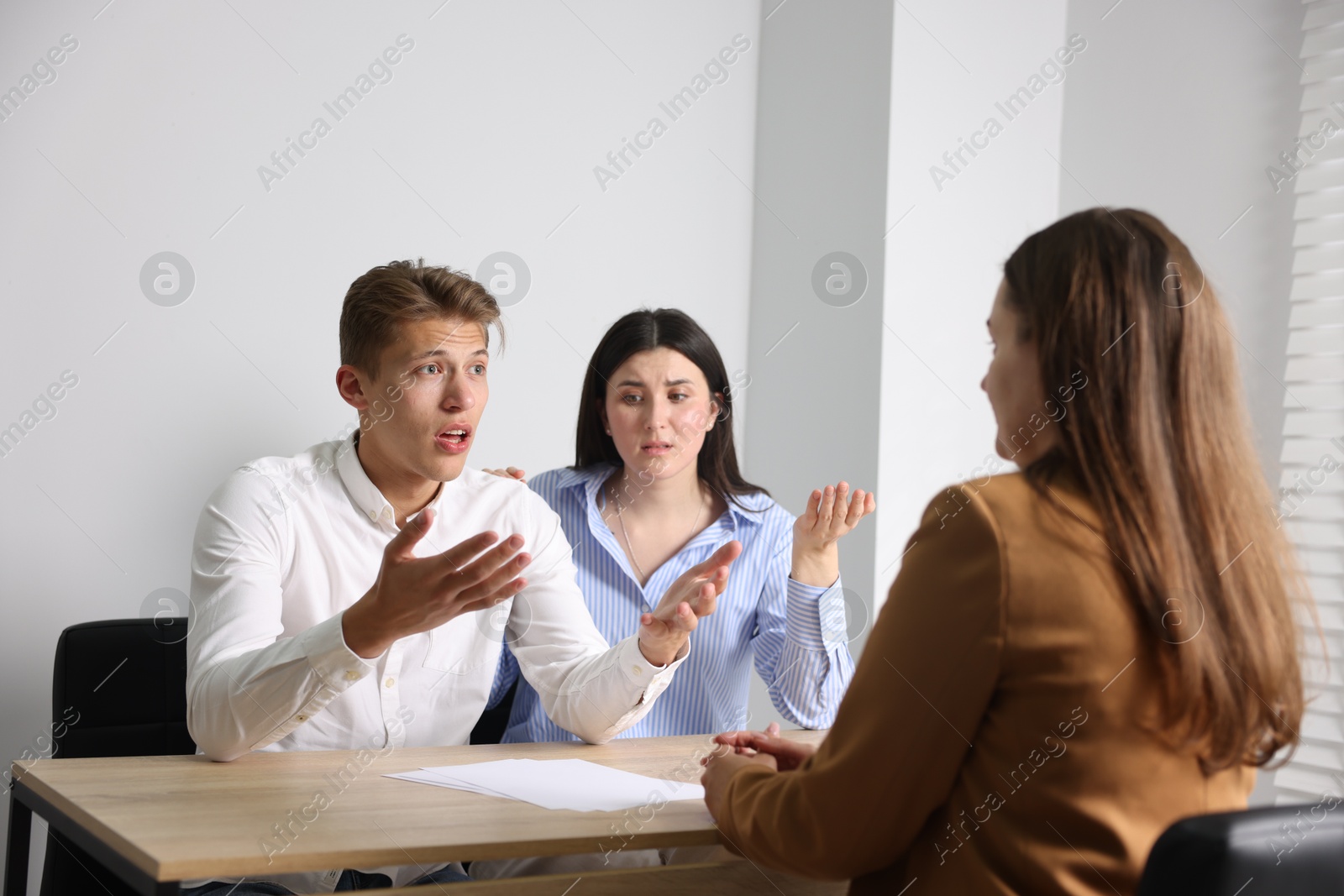 Photo of Couple complaining to woman at wooden table indoors