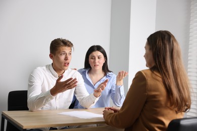 Photo of Couple complaining to woman at wooden table indoors