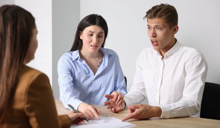 Photo of Couple complaining to woman at wooden table indoors