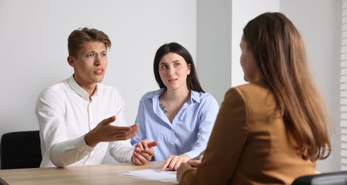 Photo of Couple complaining to woman at wooden table indoors