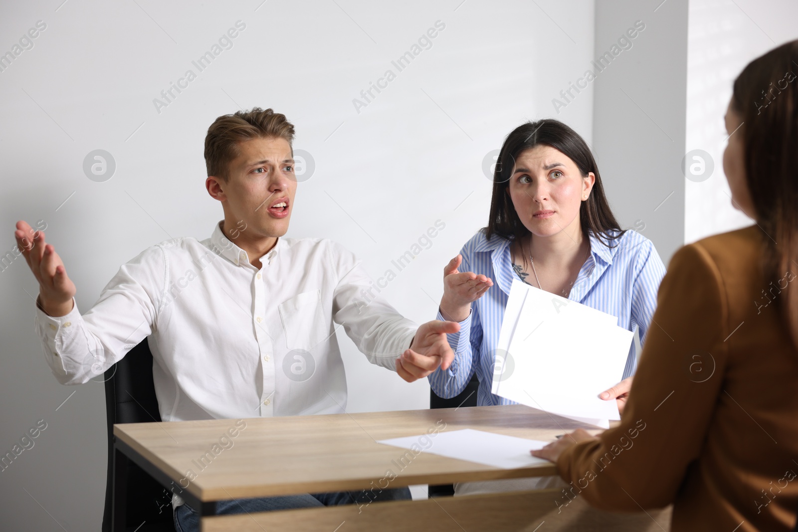Photo of Couple complaining to woman at wooden table indoors