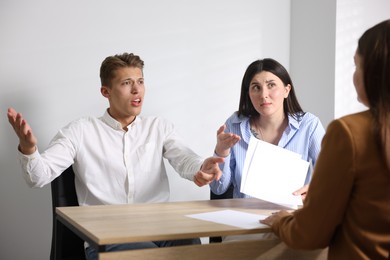 Photo of Couple complaining to woman at wooden table indoors