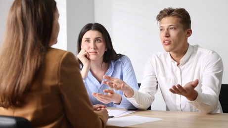 Photo of Couple complaining to woman at wooden table indoors