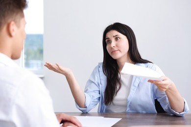 Photo of Young woman complaining to man at wooden table indoors