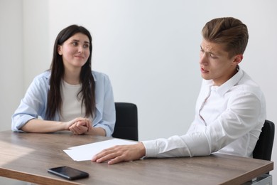 Photo of Young man complaining to woman at wooden table indoors