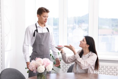 Photo of Young woman complaining to waiter about donut at table in restaurant