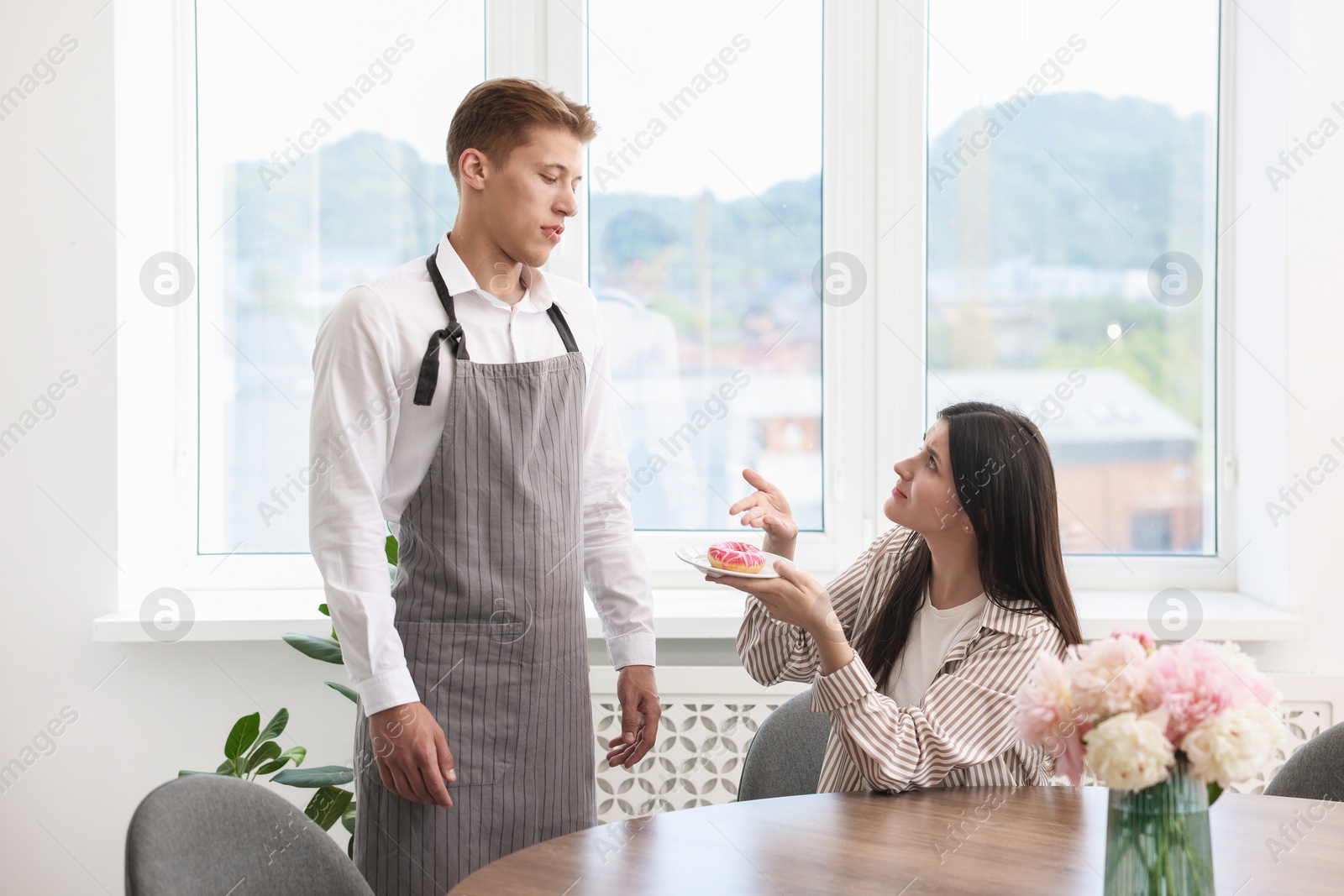 Photo of Young woman complaining to waiter about donut at table in restaurant