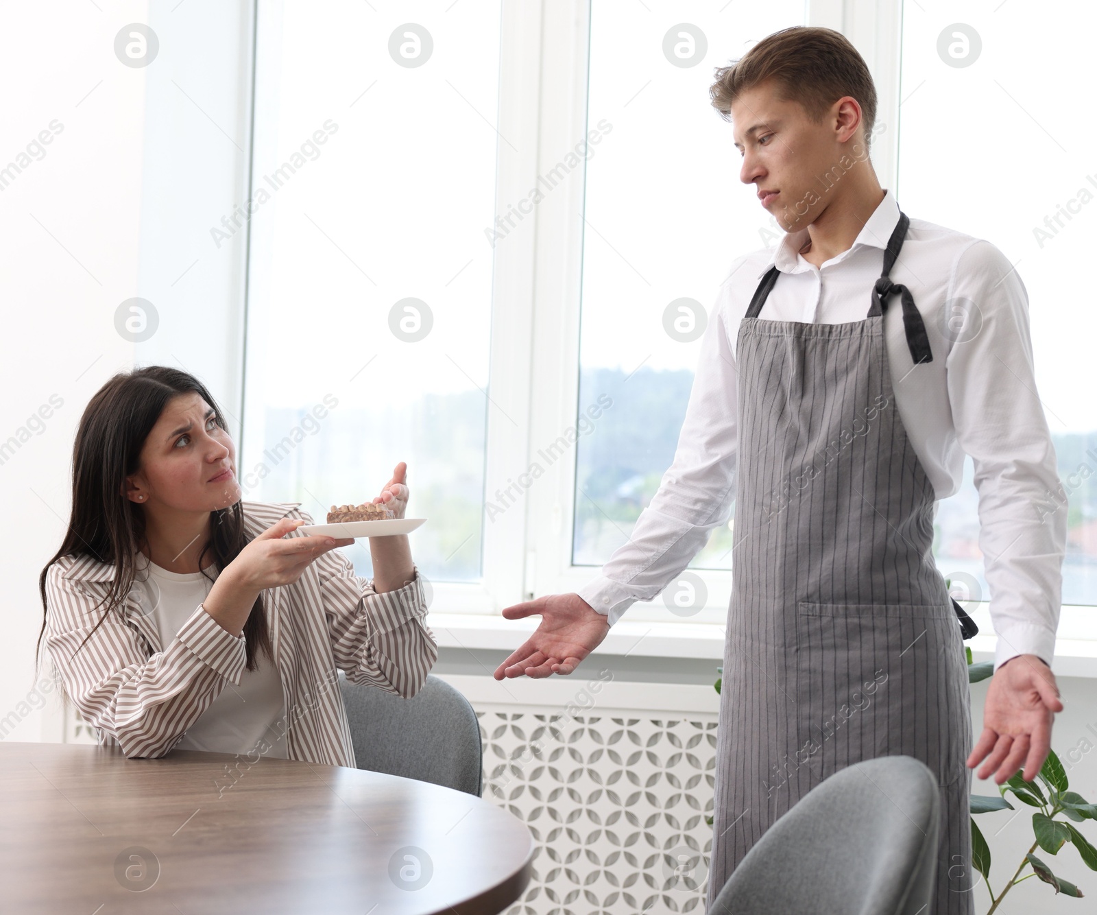 Photo of Young woman complaining to waiter about cake at table in restaurant