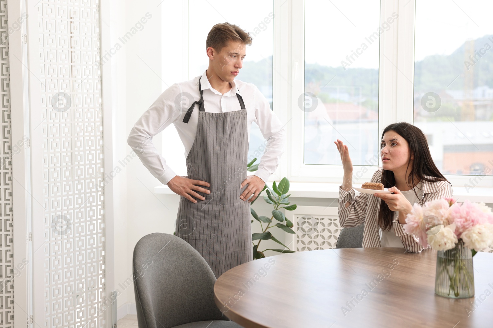 Photo of Young woman complaining to waiter about cake at table in restaurant