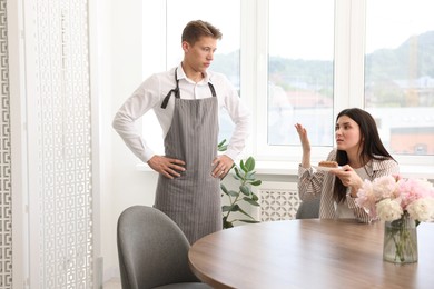 Photo of Young woman complaining to waiter about cake at table in restaurant
