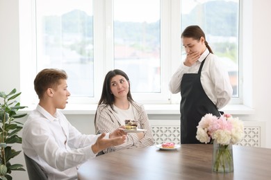 Photo of Couple complaining to waiter about cake at table in restaurant