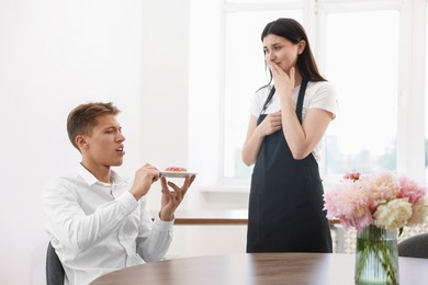 Photo of Young man complaining to waiter about donut at table in restaurant