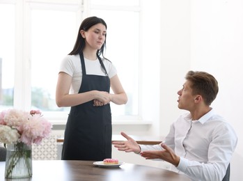 Photo of Young man complaining to waiter about donut at table in restaurant