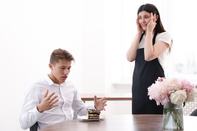 Photo of Young man complaining to waiter about cake at table in restaurant