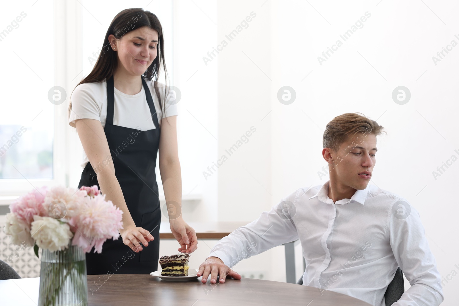 Photo of Young man complaining to waiter about cake at table in restaurant