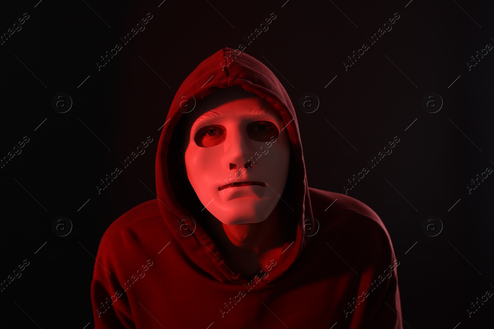 Photo of Anonymity. Masked man on dark background with red light