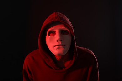 Photo of Anonymity. Masked man on dark background with red light