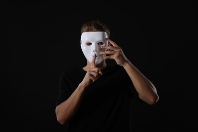 Photo of Anonymity. Man with mask showing hush gesture on dark background