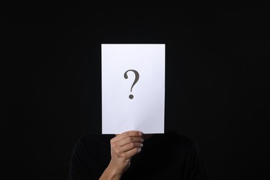 Photo of Man hiding behind paper sheet with question mark on dark background