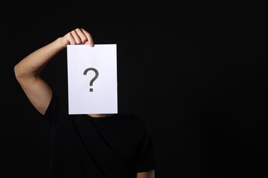 Photo of Man hiding behind paper sheet with question mark on dark background