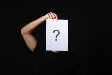 Photo of Man hiding behind paper sheet with question mark on dark background