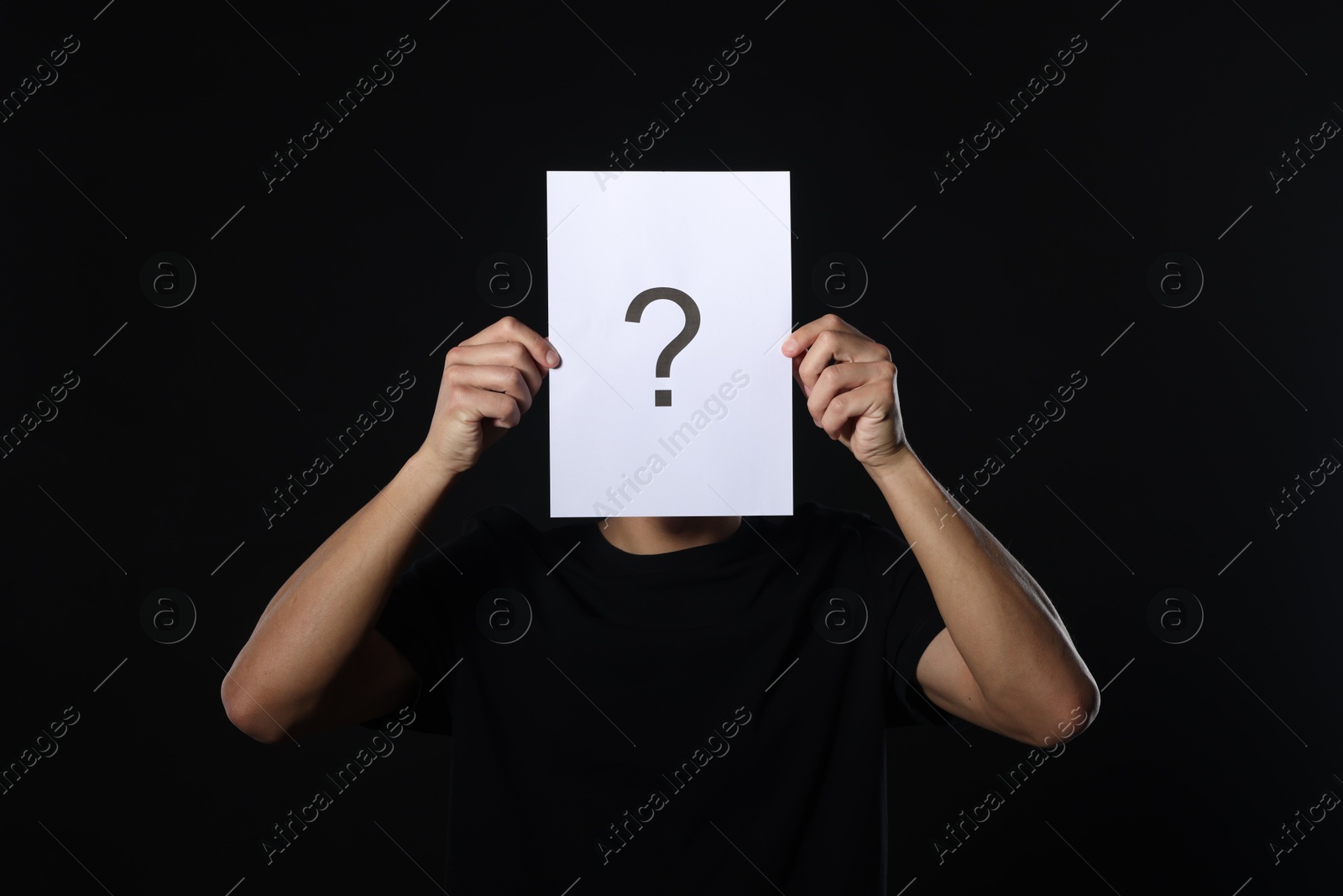Photo of Man hiding behind paper sheet with question mark on dark background