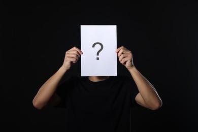 Photo of Man hiding behind paper sheet with question mark on dark background