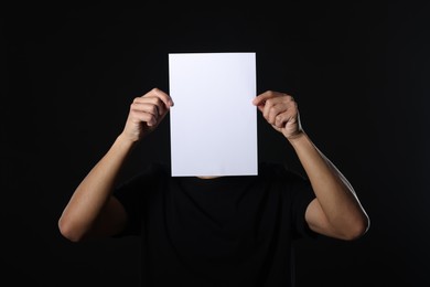 Photo of Man covering his face with paper sheet on dark background