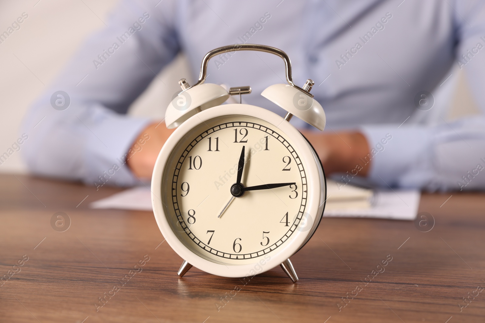 Deadline. Alarm clock and man working at wooden table, selective focus Photo of Deadline. Alarm clock and man working at wooden table, selective focus