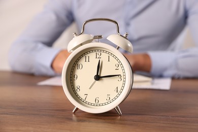 Photo of Deadline. Alarm clock and man working at wooden table, selective focus