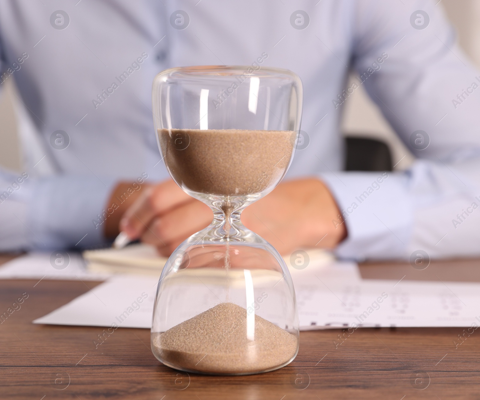 Deadline. Hourglass and man working at wooden table, selective focus Photo of Deadline. Hourglass and man working at wooden table, selective focus