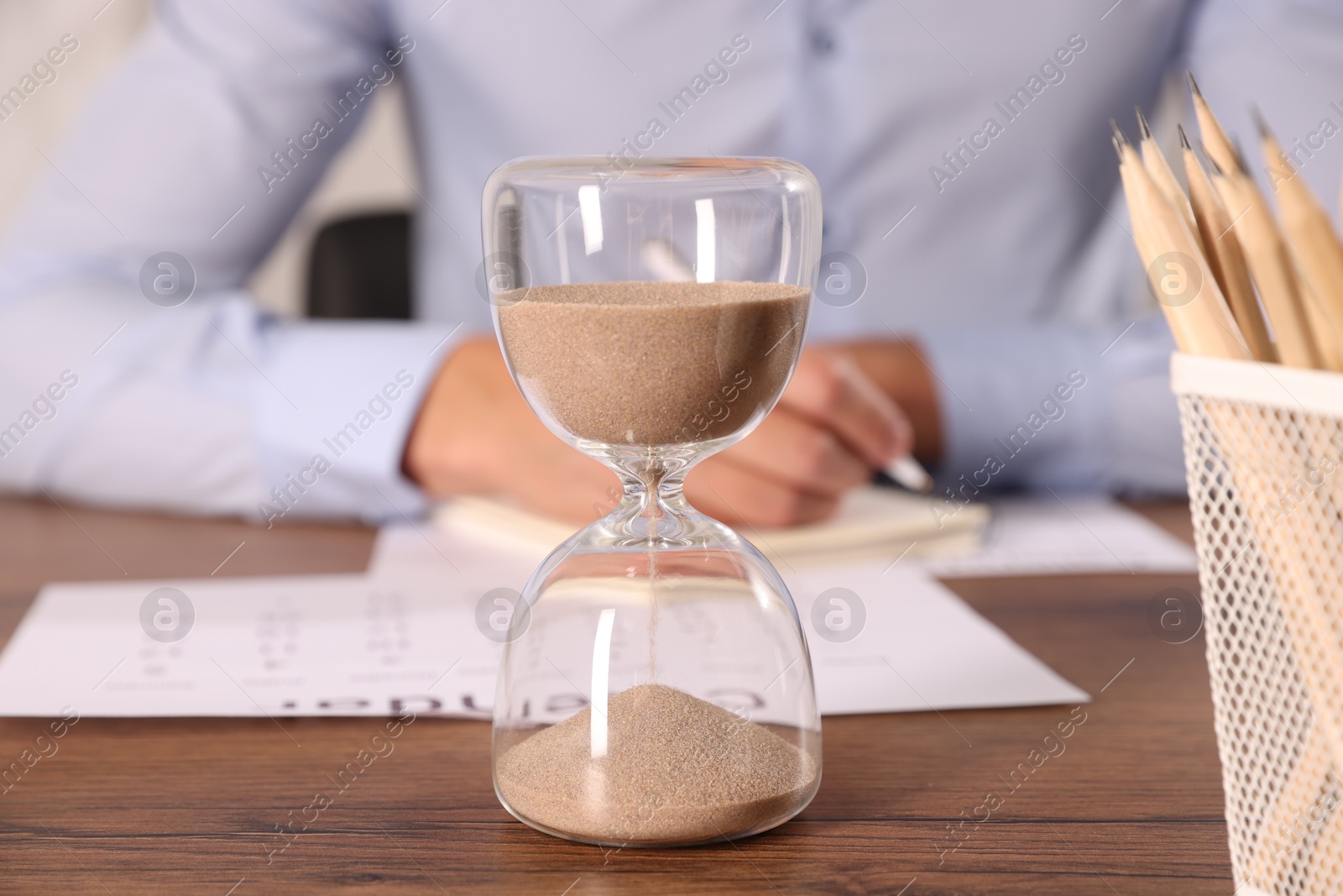Deadline. Hourglass and man working at wooden table, selective focus Photo of Deadline. Hourglass and man working at wooden table, selective focus